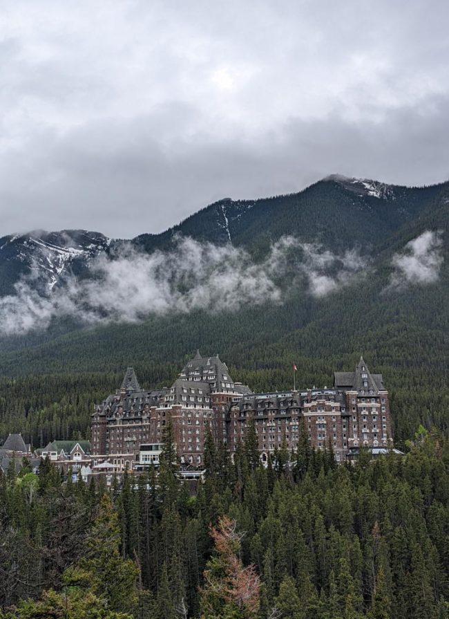 distant exterior view of the Fairmont Banff Springs with clouds and mountains in the background